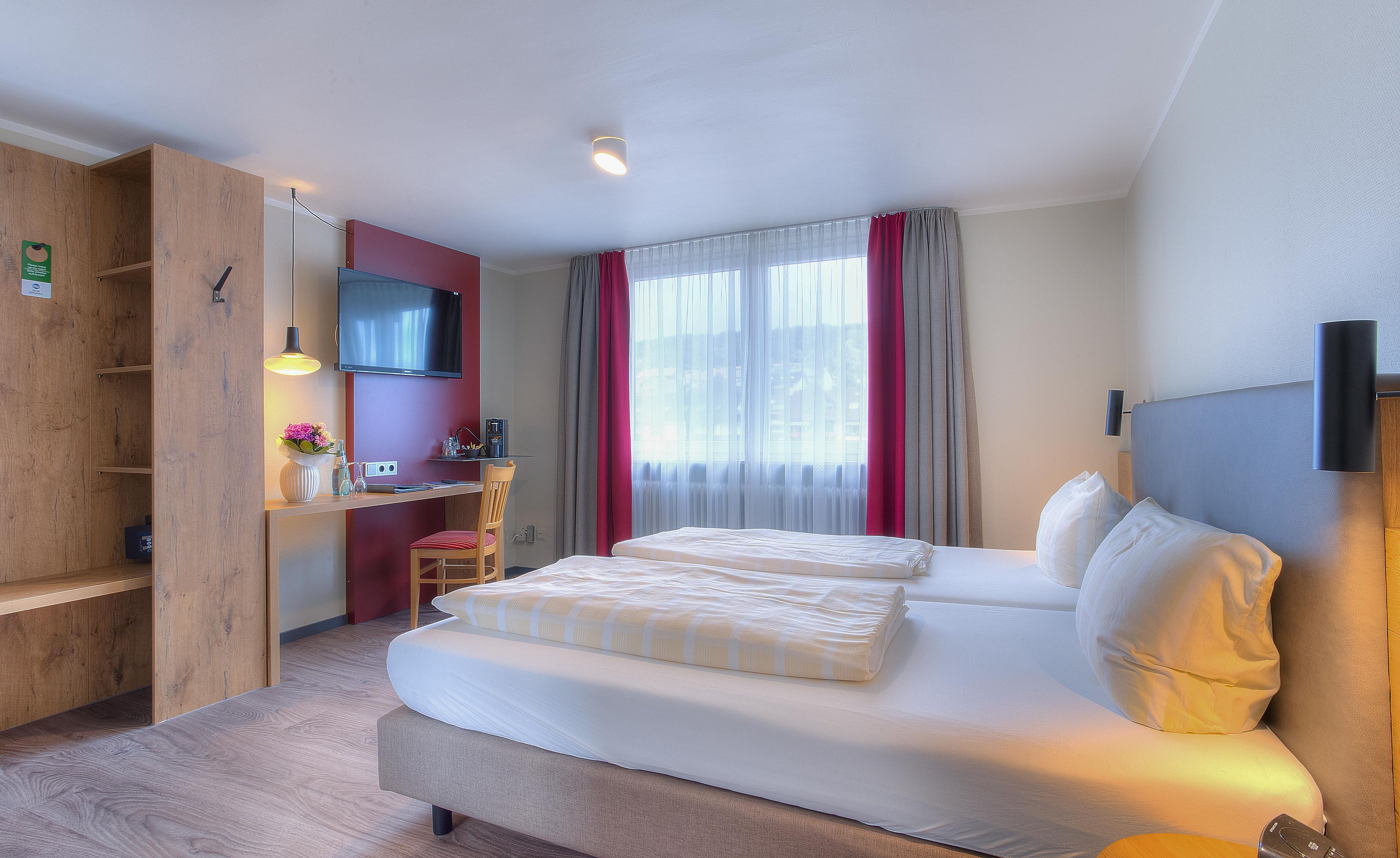 A hotel room with a bed, a desk, a TV, and a window with curtains.