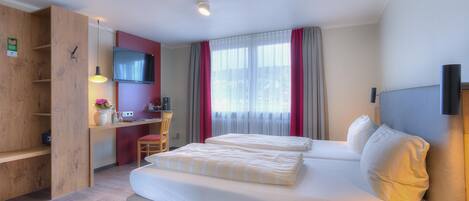 A hotel room with a bed, a desk, a TV, and a window with curtains.