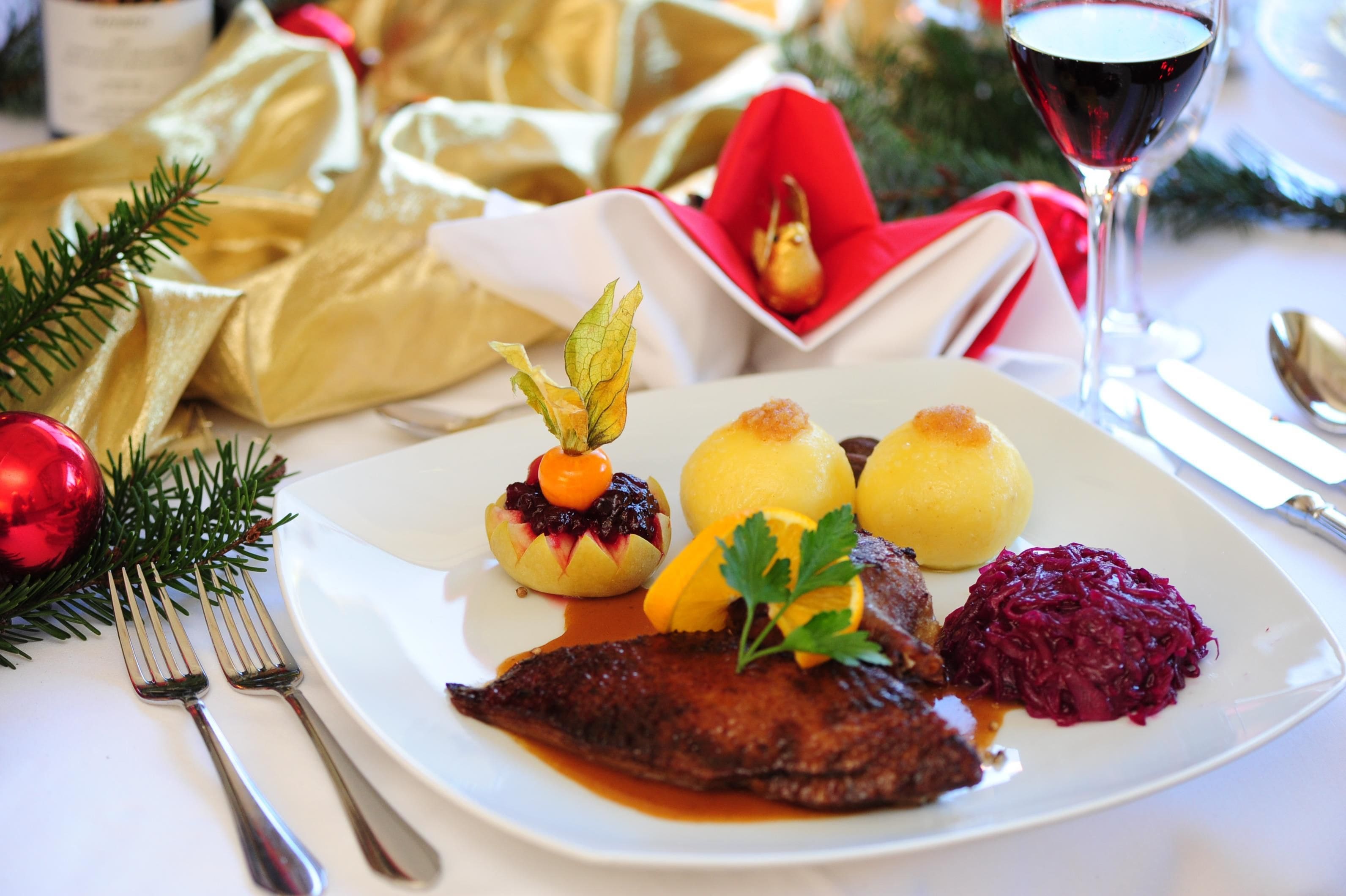 A plated meal with a fish, potatoes, and red cabbage, accompanied by a glass of red wine.