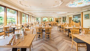 Un restaurante espacioso con mesas y sillas de madera, ventanas amplias y un techo decorativo.