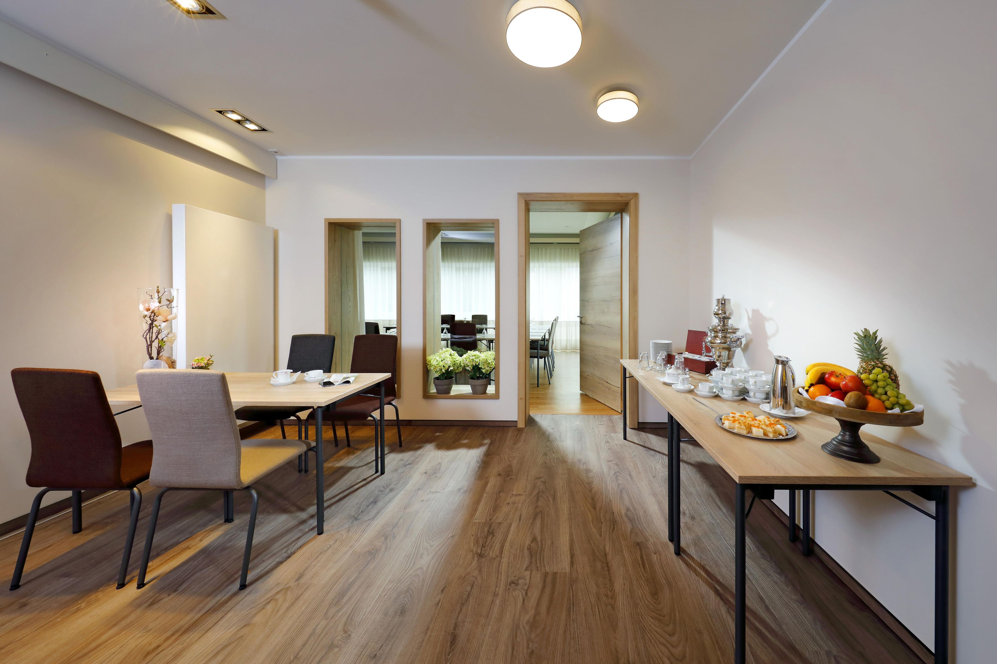 Una sala de reuniones moderna con una larga mesa, sillas y una mesa de buffet con frutas y pasteles.