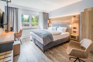 Habitación de hotel moderna con una cama grande, un escritorio, dos sillas, una ventana con cortinas y vistas a zonas verdes.