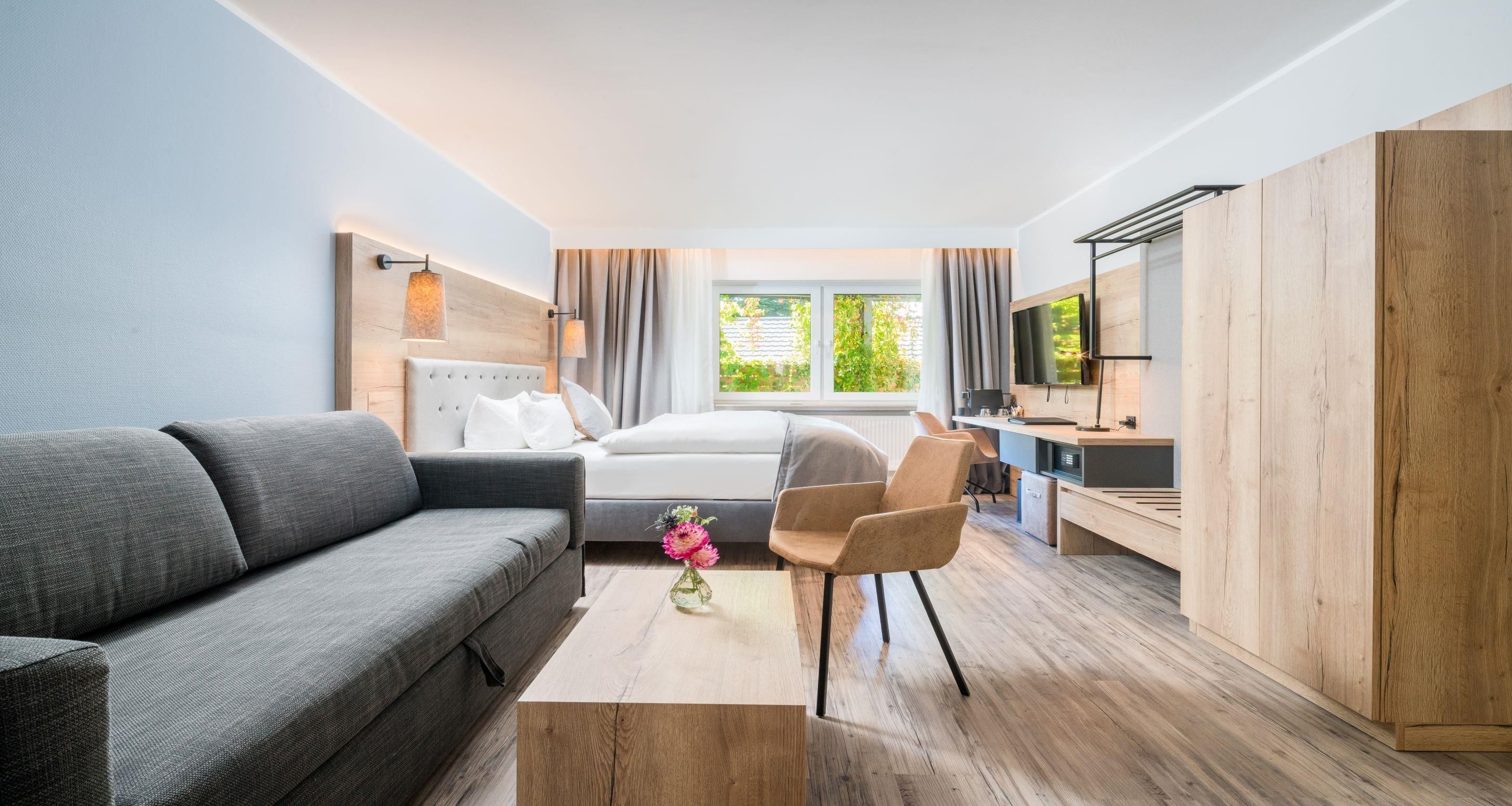 A modern hotel room with a bed, a sofa, a desk, and a television.