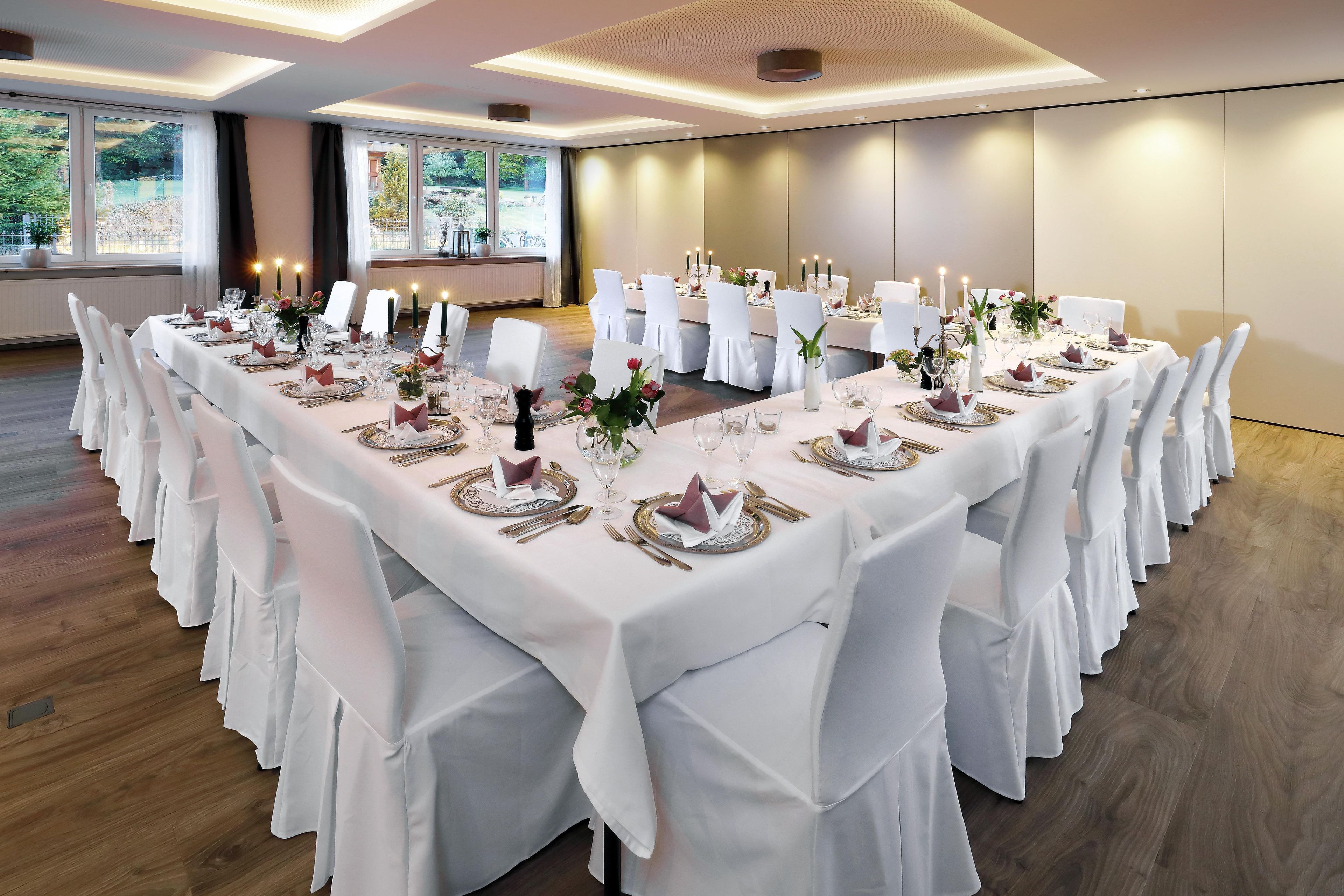 A banquet hall with round tables set for a formal event, featuring white tablecloths, gold cutlery, and floral centerpieces.