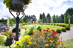 Un jardín con diversas flores, un edificio pequeño y setos bien cuidados.