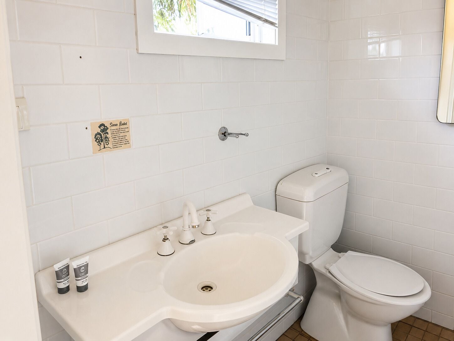 Un baño con lavamanos blanco, inodoro y ventana sobre el lavamanos.