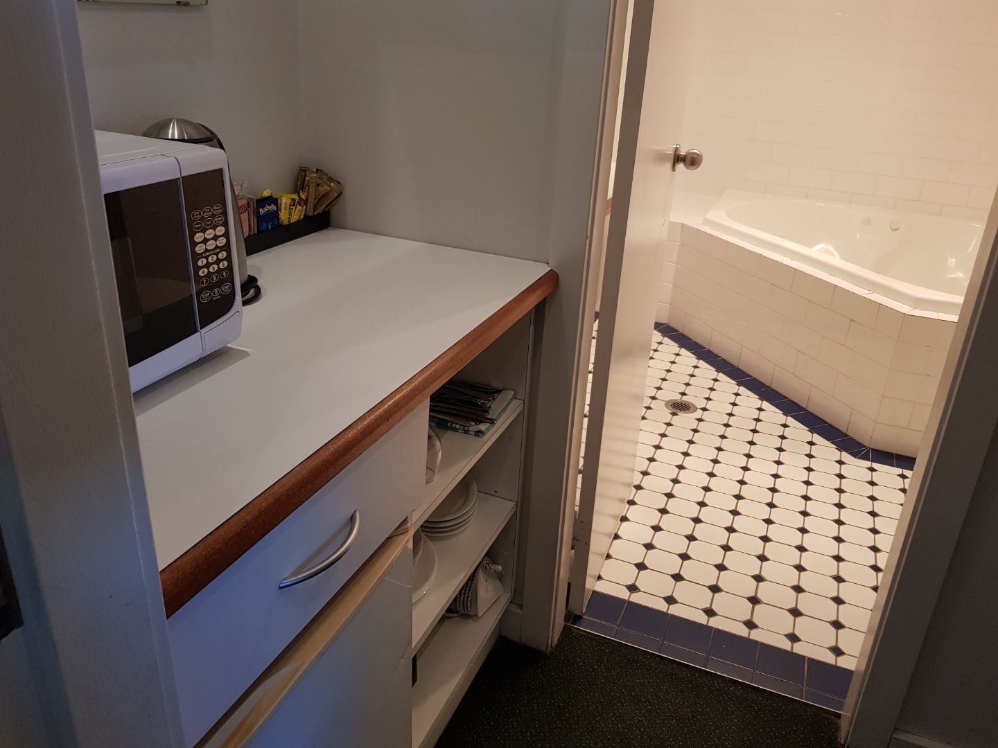 Une petite salle de bain avec un comptoir blanc, un four à micro-ondes et une petite étagère.