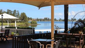 A covered outdoor seating area with tables and chairs, overlooking a lake.