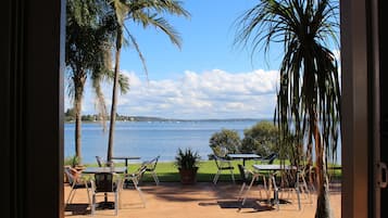 Enjoy a tranquil patio with a table, chairs, and lush greenery, overlooking a serene body of water and distant shoreline.