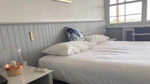 A neatly made bed with white bedding, a bedside table with a lamp, a remote control, and a book.