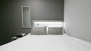Habitación de hotel con una cama grande, dos almohadas, una mesita de noche, una lámpara y un espejo montado en la pared.