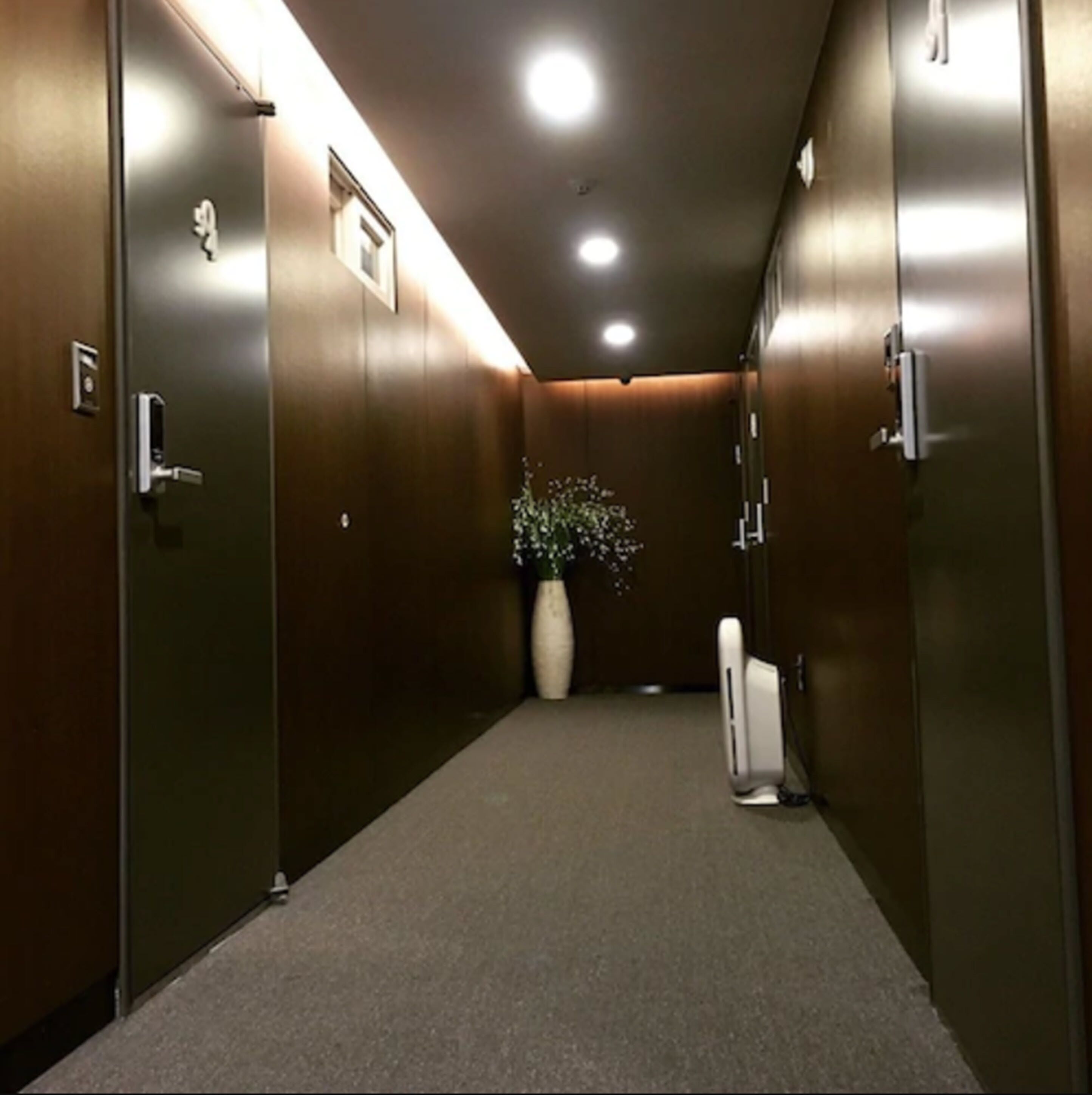 A hallway with wooden walls, a white vase with flowers, and a white device on the floor.