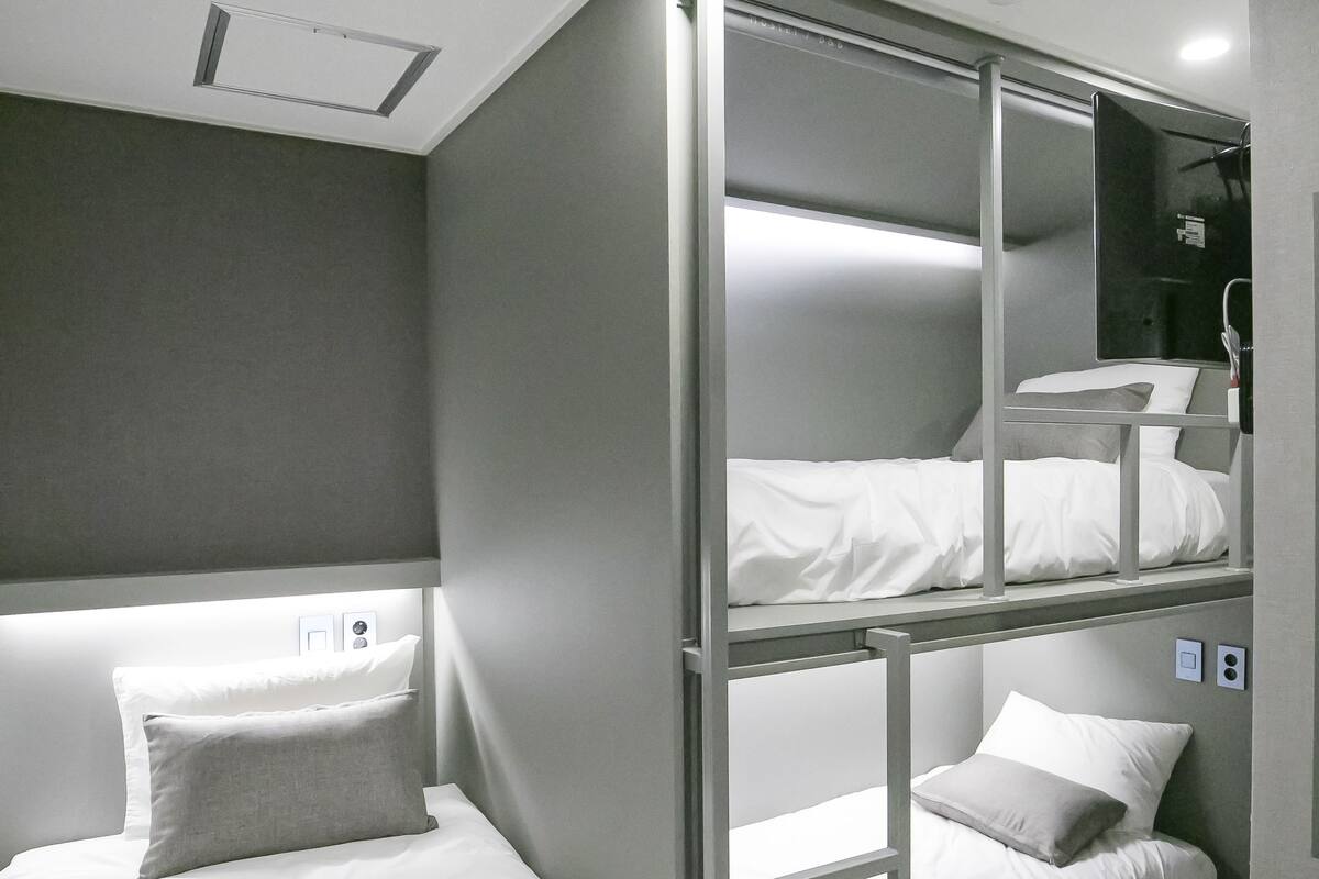 Habitación de hotel con literas, una mesita de noche y un espejo.