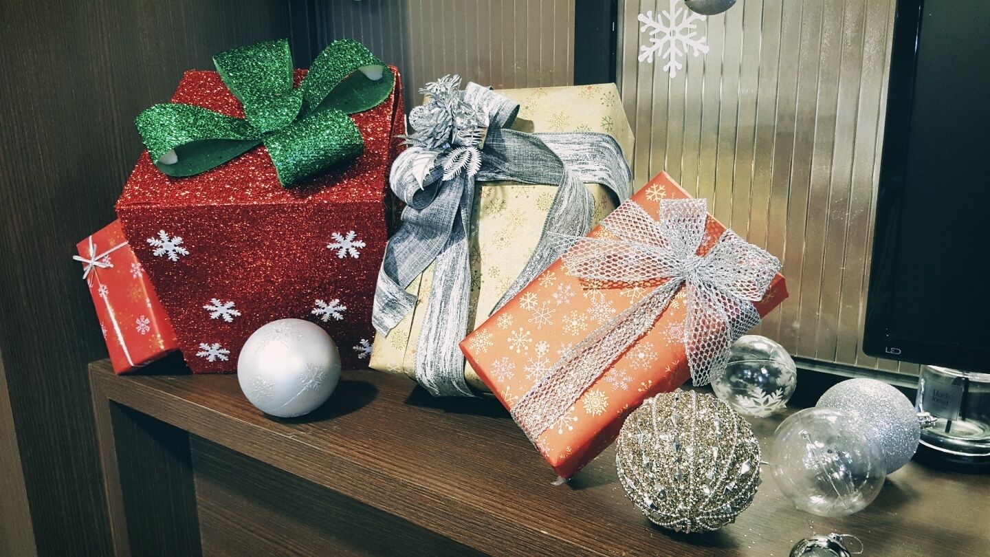Un estante de madera con varios regalos envueltos, un adorno plateado y uno transparente.