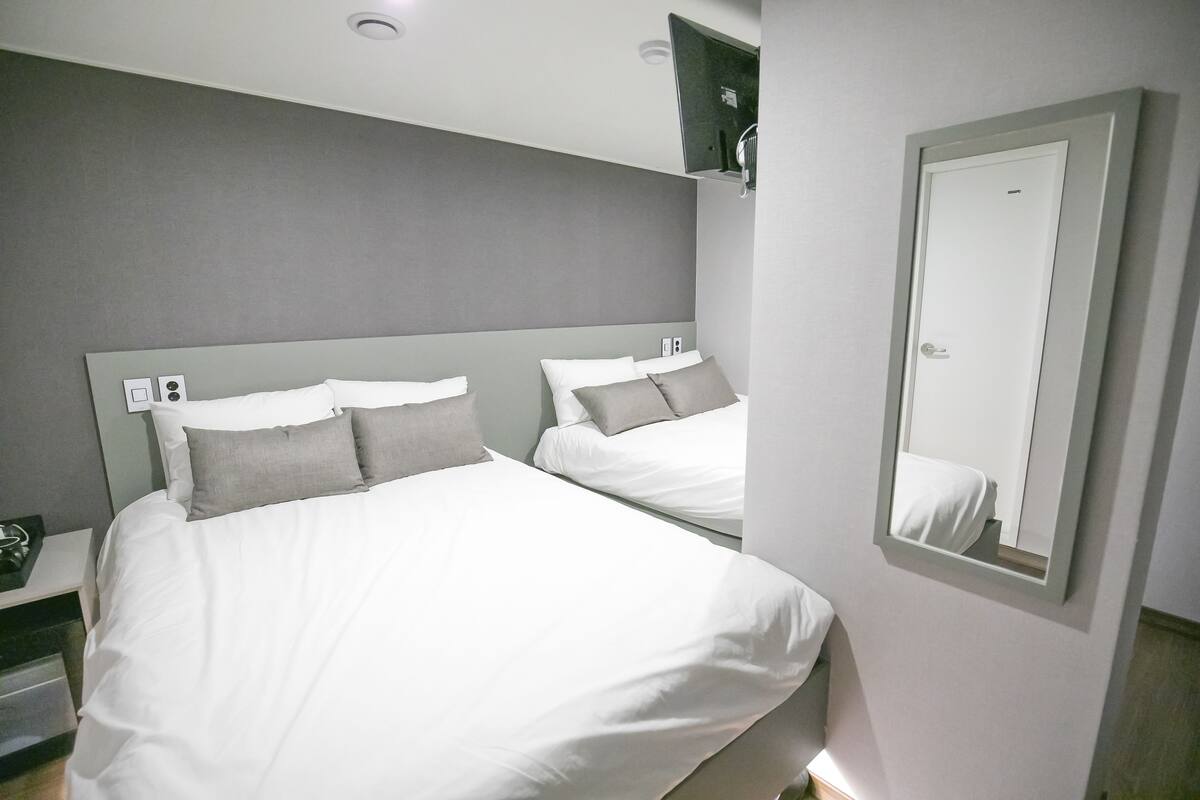 Habitación de hotel con dos camas, un espejo grande y una mesita pequeña.