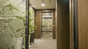 Un vestíbulo de hotel con un ascensor de vidrio, plantas en macetas y una recepción.