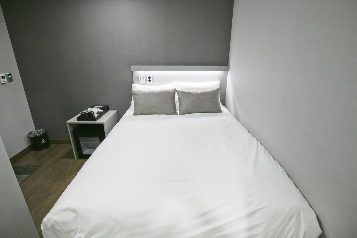 Habitación de hotel con una cama individual, una mesita de noche y una pequeña tocador.