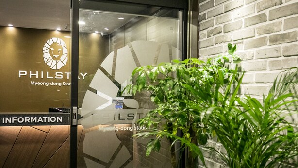 Zona de recepción con pared de vidrio, un logotipo y una planta.