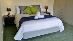 A neatly made bed with a blue blanket, white pillows, and a green pillow. There are two bedside tables with lamps, and a wardrobe with sliding doors. - Beaulieu (Coles Bay)
