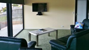 A living room with a TV mounted on the wall, a small table, and a leather sofa. - Beaulieu (Coles Bay)