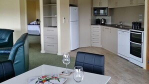 A compact kitchen with a refrigerator, microwave, and oven. There is a dining area with a table and chairs. - Beaulieu (Coles Bay)