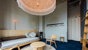 Une pièce moderne comprenant un canapé, deux chaises en bois, une petite table, un luminaire suspendu et un tapis bleu.