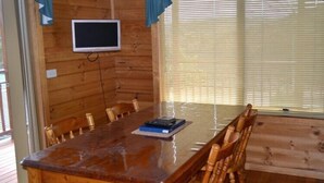 A wooden-paneled room with a large table, chairs, a television, and a window with blinds. - Coles Bay House (Coles Bay)