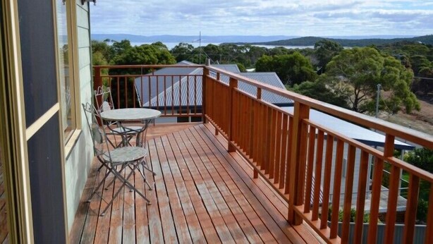 A wooden deck with a table and chairs, overlooking a landscape with trees and distant hills. - Coles Bay House (Coles Bay)