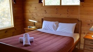 A wooden cabin bedroom with a bed, a nightstand, and a window. - Coles Bay House (Coles Bay)