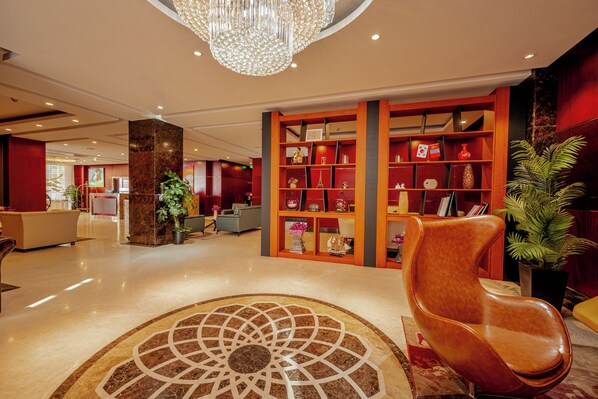 A lobby with a marble floor, a central chandelier, and a seating area with a red and brown color scheme.