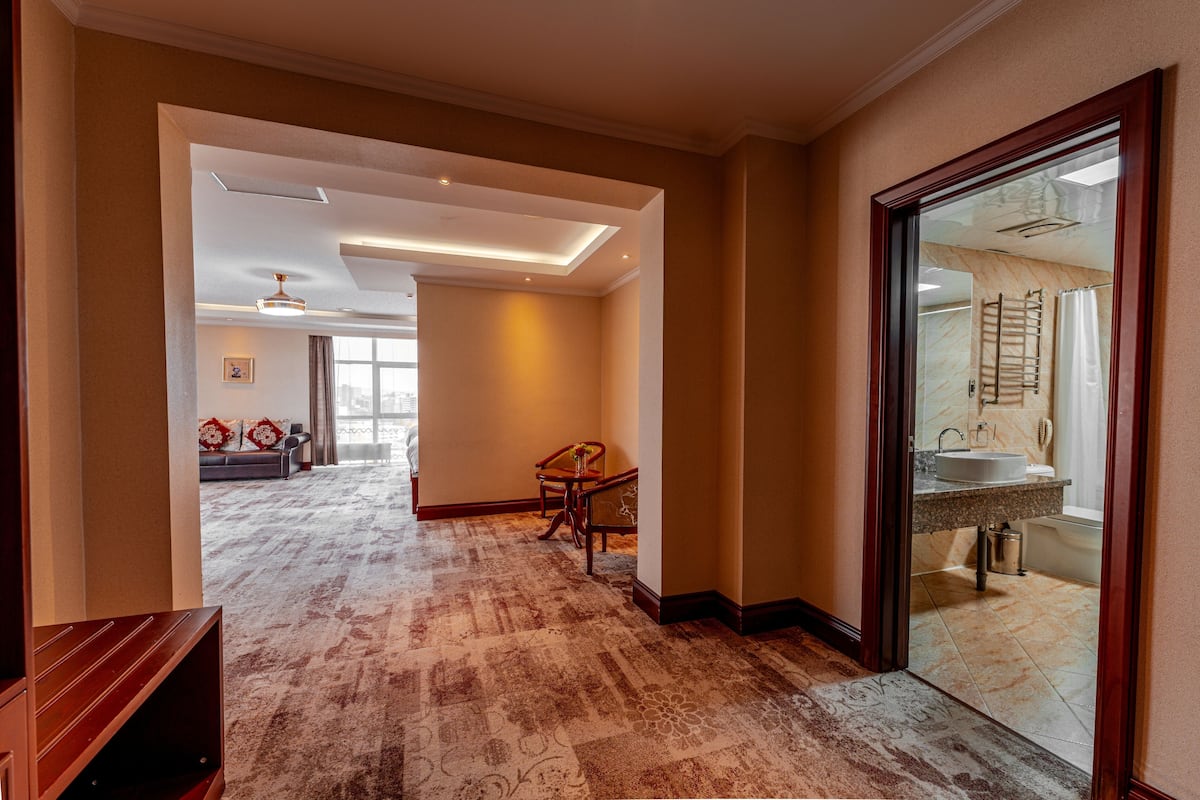 A spacious hallway with a patterned carpet, a wooden bench, and a view into a bathroom with a sink and shower.