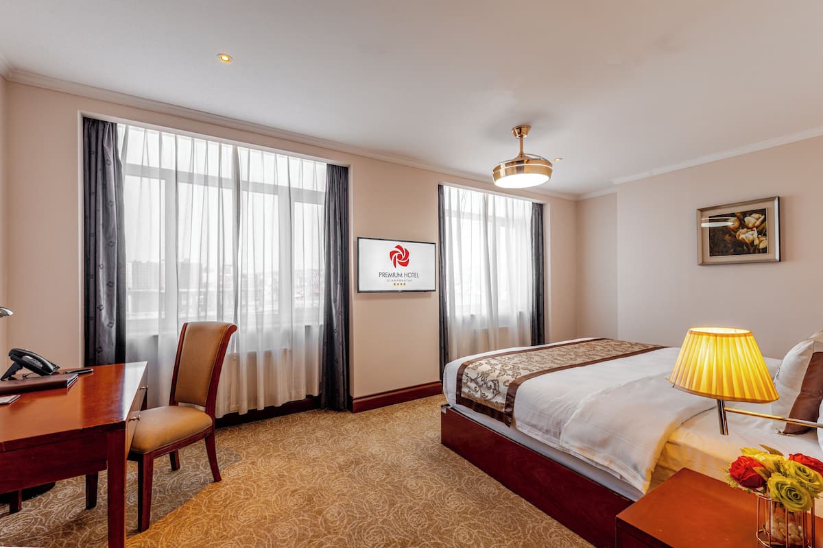 A hotel room with a bed, desk, chair, and a framed logo on the wall.