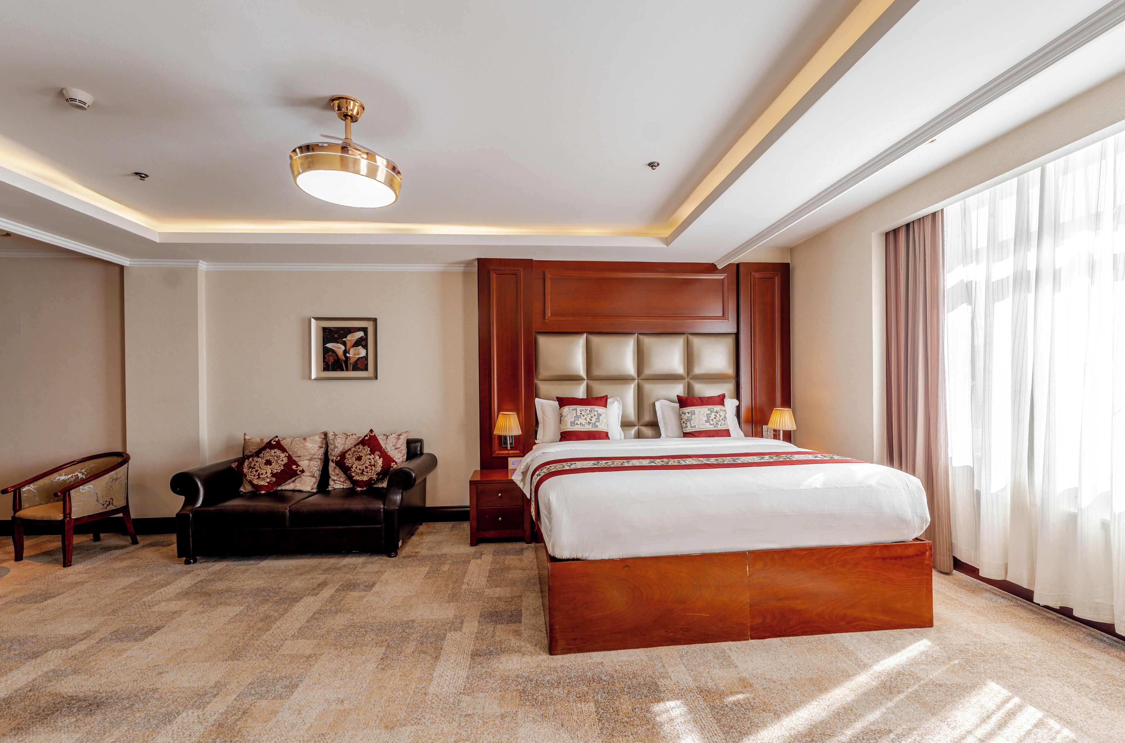 A hotel room with a large bed, a sofa, a nightstand, and a ceiling fan.