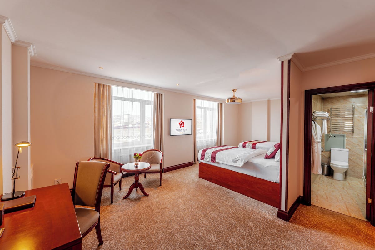 A hotel room with a bed, a desk, a chair, and a small table with a lamp.