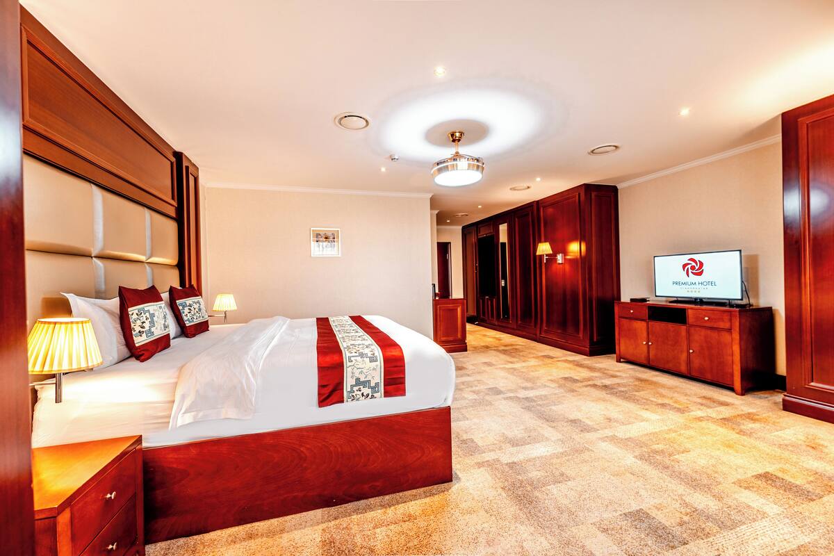 A hotel room with a large bed, wooden headboard, bedside lamps, a television, and a carpeted floor.