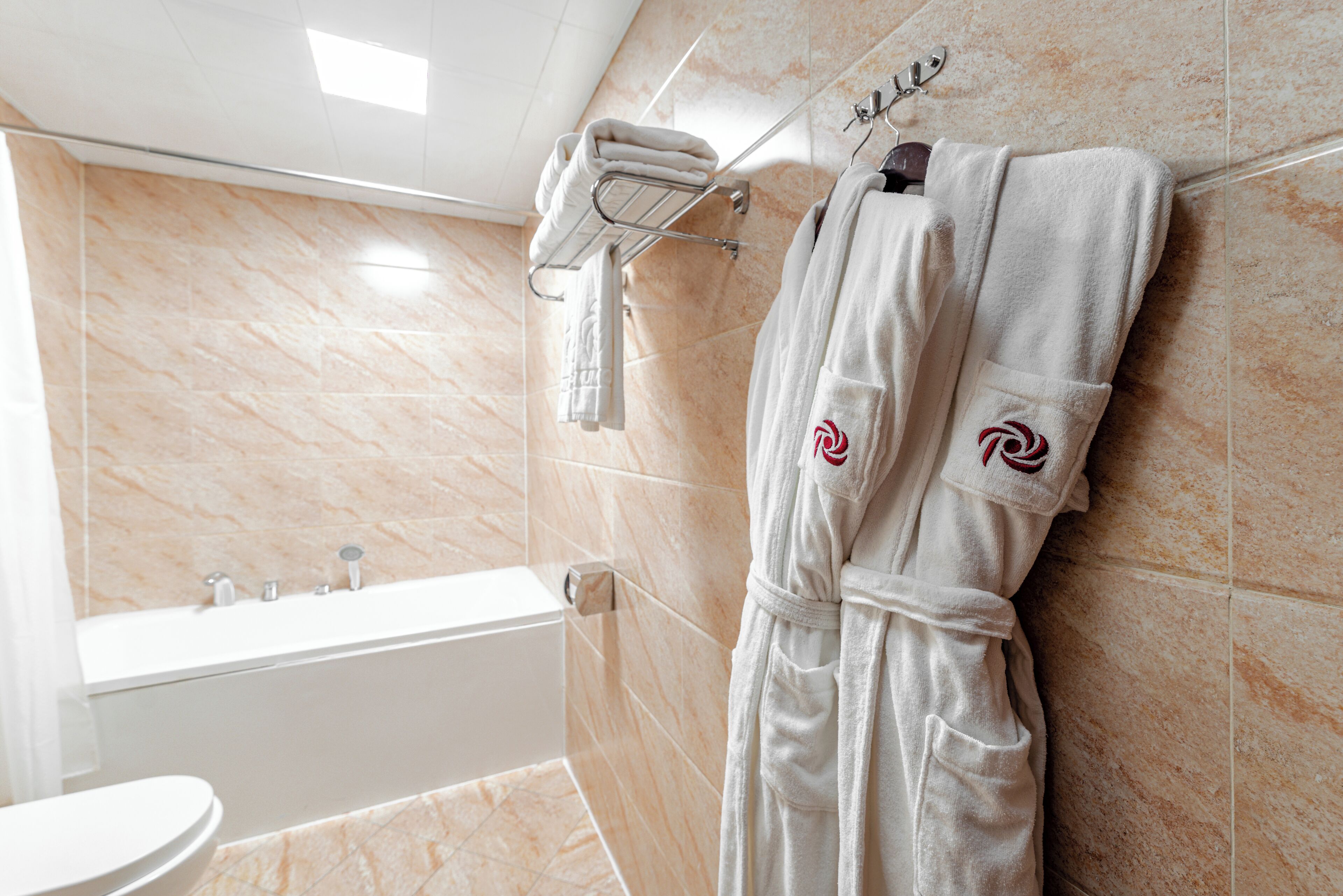 A bathroom with a bathtub, a towel rack with towels, and a robe hanging on the wall.