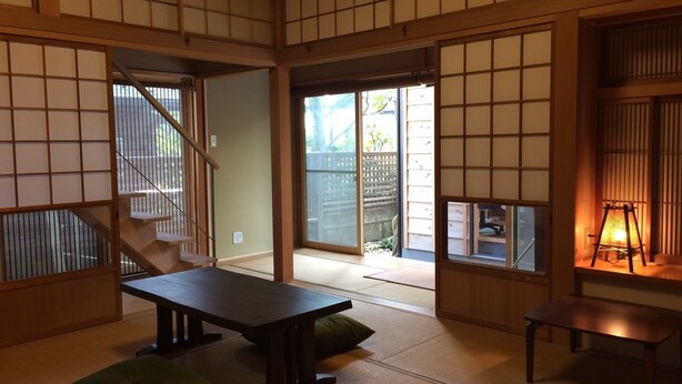 A traditional Japanese room with tatami flooring, a low table, cushions, sliding doors, and a view of the outside. - Guest House Kamakura Zen-ji - Hostel (Kamakura)