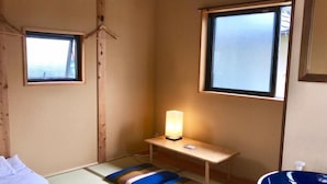 A small, cozy room with tatami flooring, a bed, a bedside table with a lamp, a window, and a blue sink. - Guest House Kamakura Zen-ji - Hostel (Kamakura)