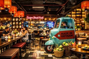 Un interior de restaurante con una camioneta azul antigua con la leyenda 'MADE IN VIETNAM' y un letrero de neón que dice 'Saigon Street Food'.
