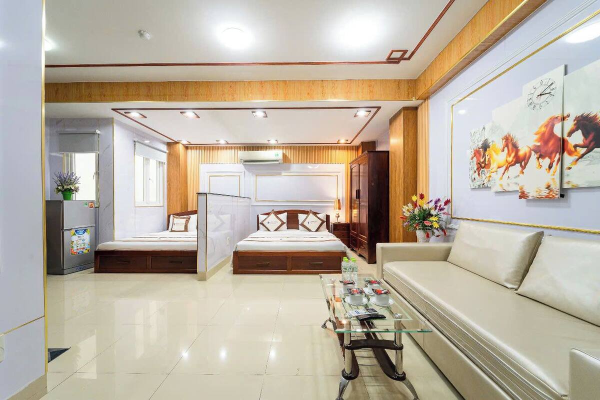 A modern hotel room with a bed, a sofa, a glass coffee table, and a wall-mounted TV.