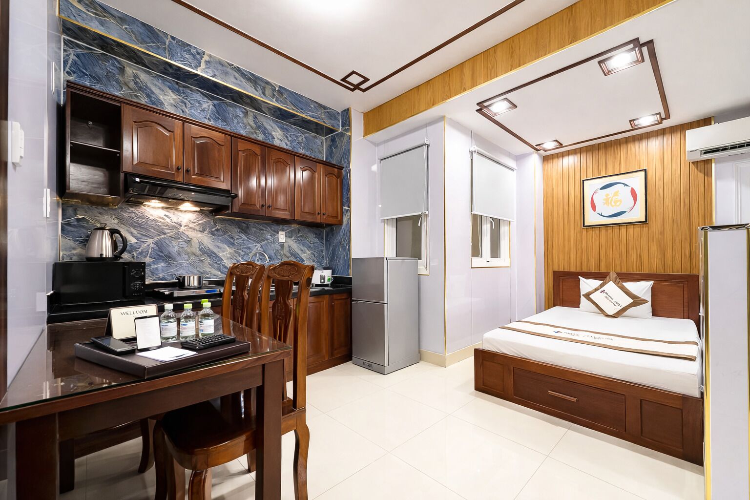 A compact hotel room with a kitchen area, a dining table, and a bed.