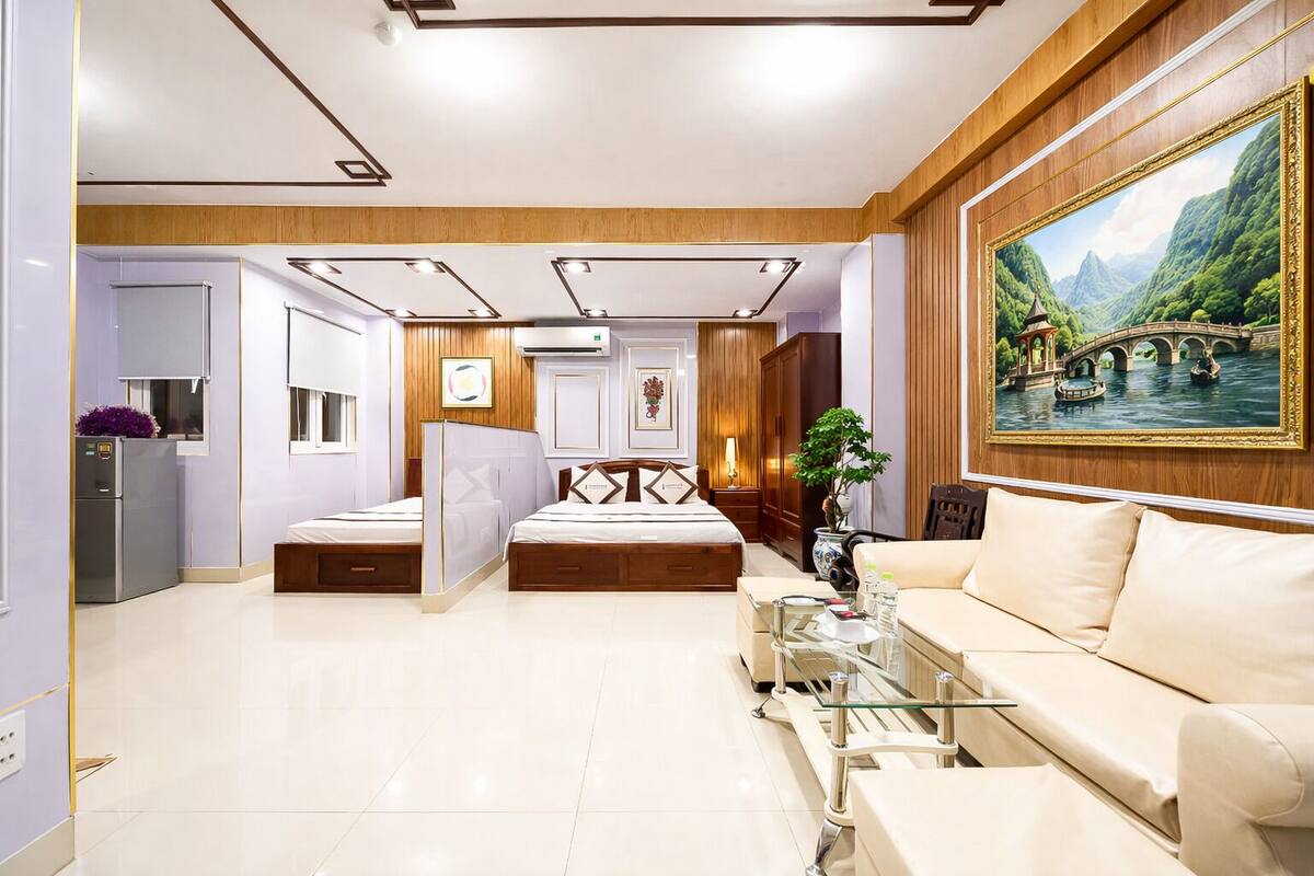 A modern hotel room with a bed, a sofa, a glass coffee table, and a painting of a bridge over a river.