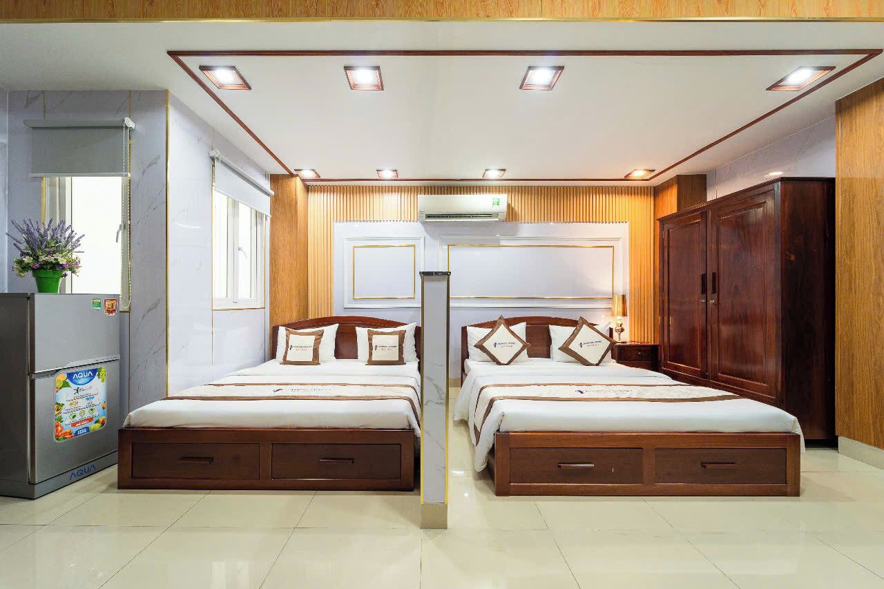 Habitación de hotel con dos camas, un armario de madera, una nevera pequeña y una ventana con persianas.