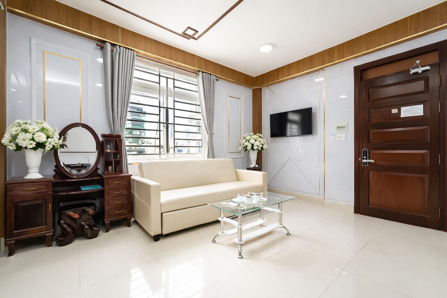 Un salon moderne avec un canapé, une table basse en verre, un téléviseur fixé au mur et une porte en bois.