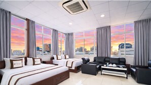 A hotel room with a large bed, two smaller beds, a sofa, and a coffee table. The room has large windows with a city view. - Diamond Luxury Ben Thanh (Ho Chi Minh City)