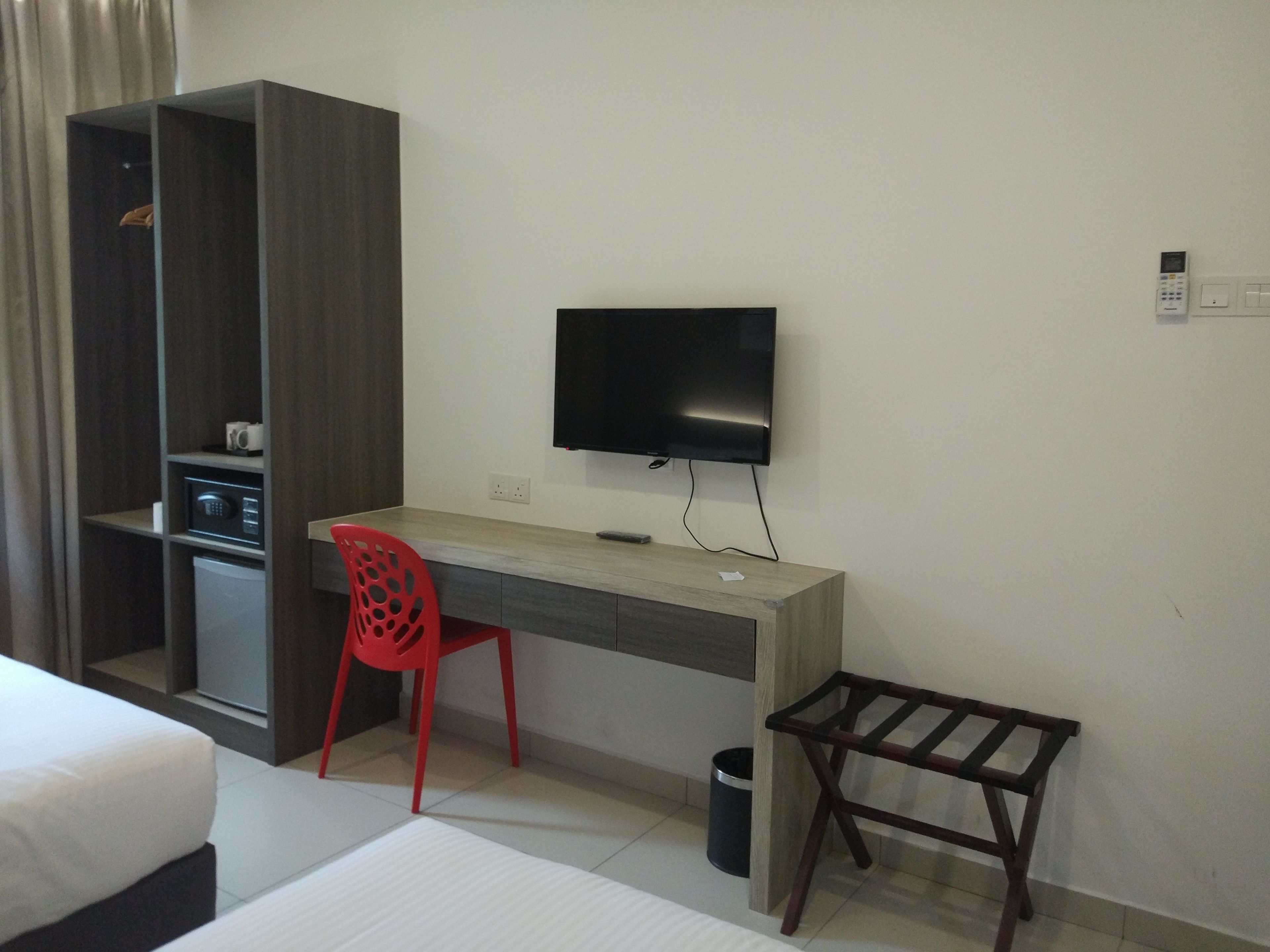 A hotel room with a bed, a desk with a chair, a TV, a wardrobe, and a small table.