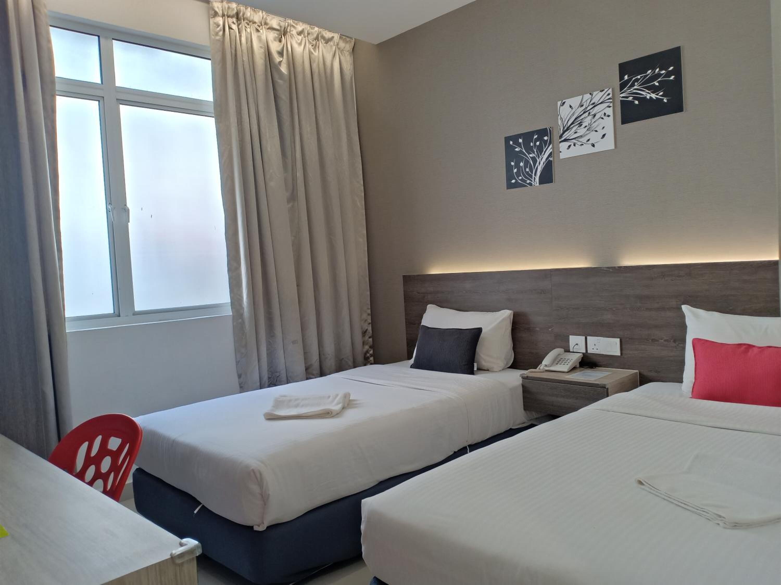A hotel room with two beds, a desk, a chair, and a window with curtains.