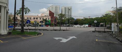 A street intersection with a large building in the background, palm trees, and a clear sky.