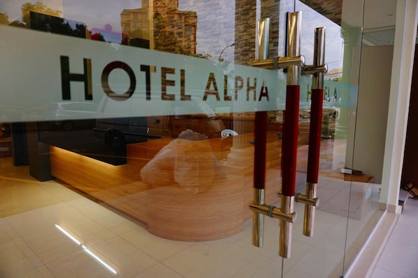 A hotel reception area with a glass door and a sign that reads "HOTEL ALPHA". - Hotel Alpha (Bukit Mertajam)