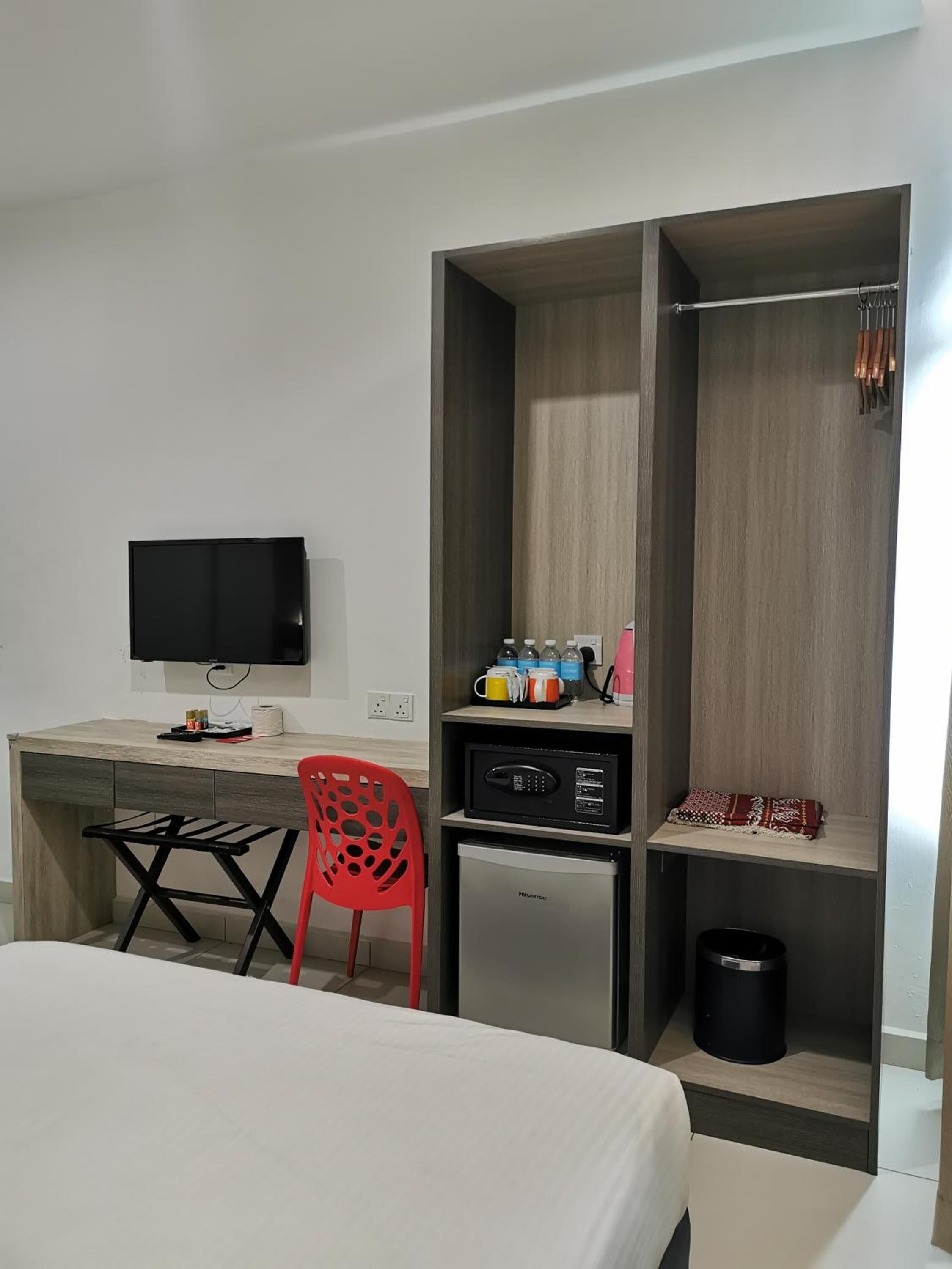 Ein Hotelzimmer mit einem Bett, einem Schreibtisch mit Flachbildfernseher, einem roten Sessel, einer Mikrowelle, einem kleinen Kühlschrank und einem Regal mit Pflegeprodukten.